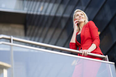 Blond businesswoman wearing red suit and using smartphone - JSMF01459