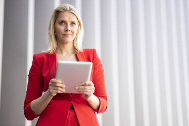 Blond businesswoman wearing red suit and using digital tablet - JSMF01461