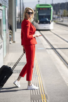 Blonde Geschäftsfrau im roten Anzug, die auf den nächsten Zug wartet - JSMF01469