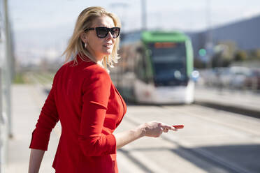 Blonde Geschäftsfrau im roten Anzug, die auf den nächsten Zug wartet - JSMF01470