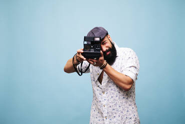 Bearded young man in studio taking picture with instant camera - DGOF00486