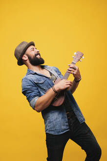 Leidenschaftlicher junger Mann im Studio spielt Ukulele - DGOF00493