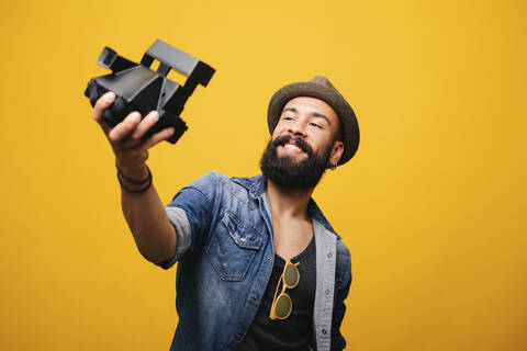 Bärtiger junger Mann im Studio macht Selfie mit Sofortbildkamera, lizenzfreies Stockfoto