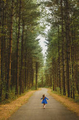 Ein kleines Kind steht allein auf einem von Bäumen gesäumten Weg mit weit geöffneten Armen - CAVF75448