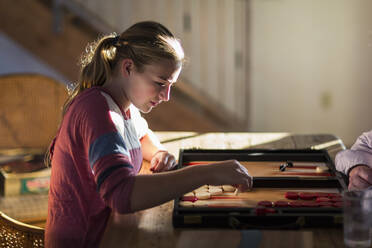 Profile of 13 year old girl at sunset playing board game - MINF13833