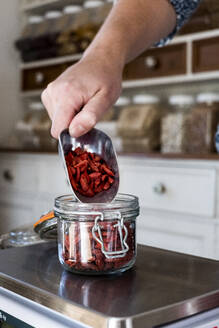 Nahaufnahme einer Person, die Goji-Beeren in einem Glasgefäß auf einer Küchenwaage wiegt. - MINF13879