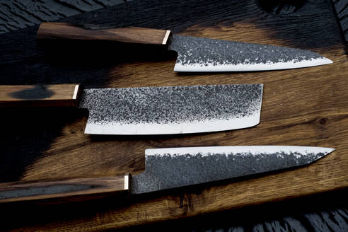 Nahaufnahme von drei handgefertigten Messern auf einem hölzernen Schneidebrett. - MINF14000