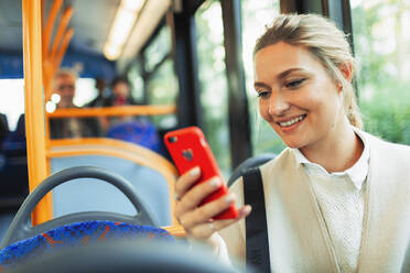 Lächelnde junge Frau benutzt ihr Smartphone im Bus - HOXF05032