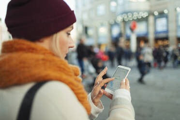 Junge Frau benutzt GPS auf einem Smartphone auf einer städtischen Straße - HOXF05035