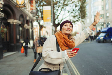 Woman with smart phone hailing taxi on urban street - HOXF05043