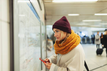 Junge Frau mit Smartphone prüft U-Bahn-Plan - HOXF05051