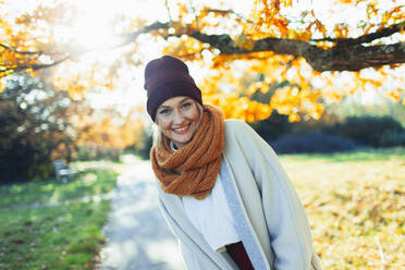 Portrait glückliche junge Frau in Strumpfmütze und Schal in sonnigem Herbstpark - HOXF05054