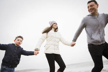 Happy boy with Down Syndrome running on beach with father and sister - HOXF05086