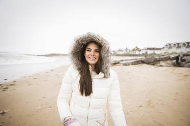Portrait happy carefree teenage girl in fur jacket on ocean beach - HOXF05089
