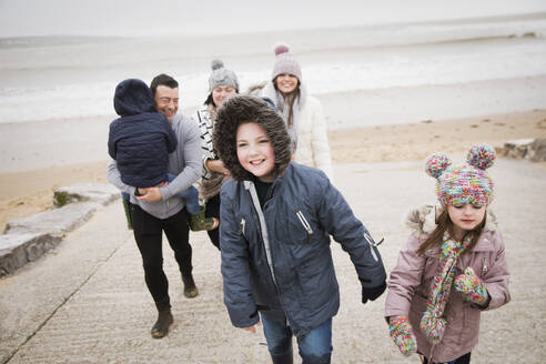 Glückliche Familie in warmer Kleidung geht die Strandrampe hinauf - HOXF05098