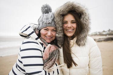 Portrait glückliche Mutter und Tochter in warmer Kleidung am Strand - HOXF05102