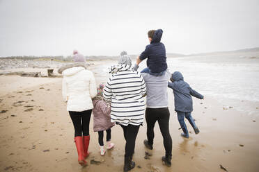 Family in warm clothing walking on winter ocean beach - HOXF05103