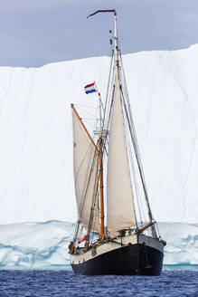 Schiff mit niederländischer Flagge, das auf dem Atlantik an einem Eisberg vorbeifährt Grönland - HOXF05135