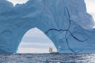 Segelboot unter majestätischem Eisbergbogen Atlantik Grönland - HOXF05140