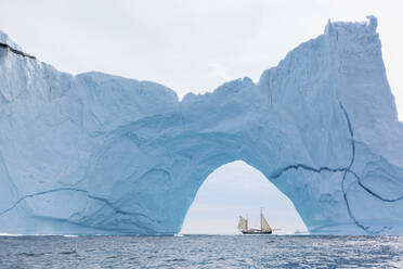 Ein Schiff fährt hinter einer majestätischen Eisbergformation auf dem Atlantik in Grönland - HOXF05162