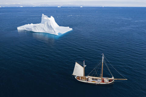 Schiff fährt an einem majestätischen Eisberg auf dem sonnigen blauen Atlantik vorbei Grönland, lizenzfreies Stockfoto