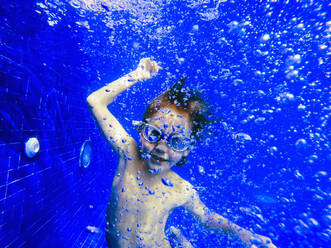 Porträt verspielter Junge schwimmt unter Wasser in blauem Schwimmbad - HOXF05192