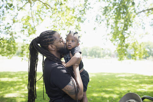 Vater mit langen Zöpfen küsst sein Kleinkind im Park - HOXF05197