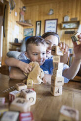 Mother helps her son build a tall tower out of wooden blocks. - CAVF75527