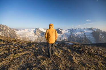 Rear view of hiker walking on mountain summit in yellow jacket. - CAVF75533
