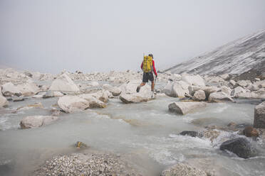 Hiker uses boulders to cross river. - CAVF75539