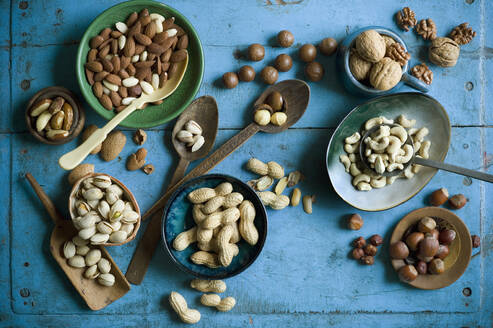 Overhead view of various nuts in bowls and on spoons on blue rustic table - ASF06581