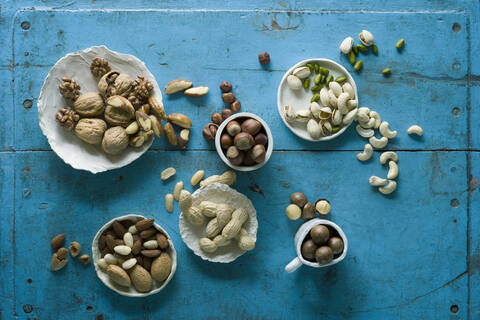 Overhead view of various nuts in bowls on blue rustic table stock photo