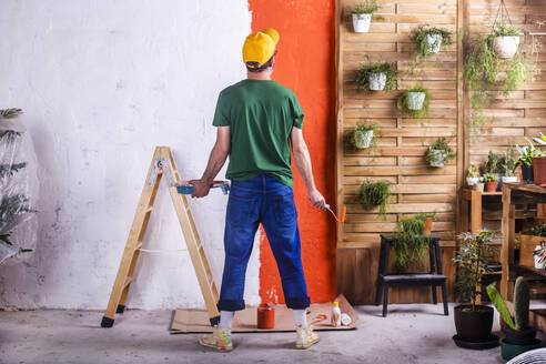 Rear view of man painting orange wall in his garden terrace - RTBF01420