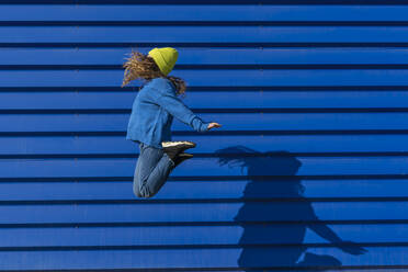 Teenager-Mädchen springt in die Luft vor blauem Hintergrund - ERRF02697