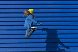 Teenage girl jumping in the air in front of blue background - ERRF02697