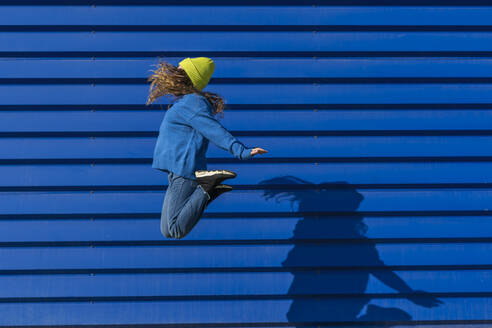 Teenager-Mädchen springt in die Luft vor blauem Hintergrund - ERRF02697