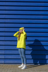 Teenager-Mädchen, das vor einem blauen Hintergrund steht und mit Kopfhörern Musik hört - ERRF02699