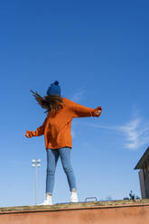 Moving teenage girl standing on wall against sky - ERRF02706