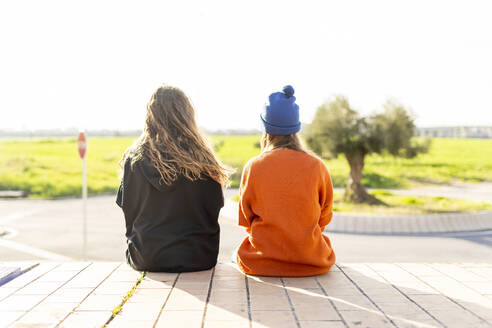 Rückenansicht von zwei Teenagermädchen, die nebeneinander im Freien sitzen - ERRF02717