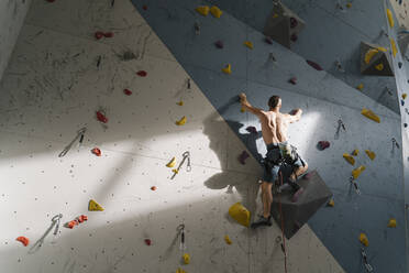 Mann ohne Hemd klettert in einer Kletterhalle an der Wand - AHSF01949