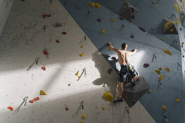 Shirtless man climbing on the wall in climbing gym - AHSF01949