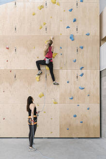 Frau mit Seil, die ihren Partner an der Wand in einer Kletterhalle sichert - AHSF01959