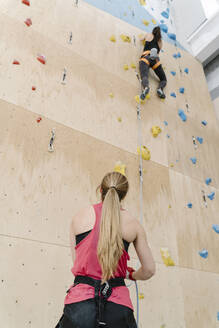 Frau mit einem Seil, das einen Partner an der Wand in einer Kletterhalle sichert - AHSF01961
