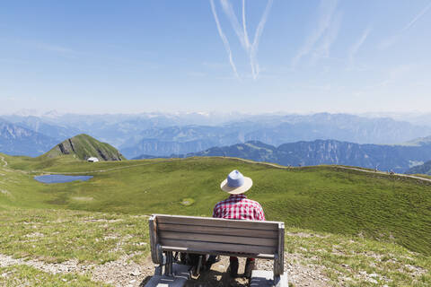 Schweiz, Kanton St. Gallen, Mann ruht sich auf Bank aus und schaut auf die Berge, lizenzfreies Stockfoto