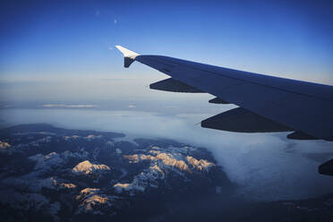 Frankreich, Auvergne-Rhone-Alpes, Flügel eines Airbus A321 im Flug über die europäischen Alpen und den Genfer See in der Morgendämmerung - RORF02015