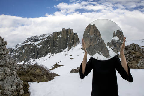 Frau, die ihren Kopf mit einem Spiegel bedeckt, der die Sella-Gruppe im Winter reflektiert, Dolomiten, Südtirol, Italien, lizenzfreies Stockfoto