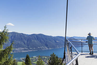 Hiker standing on viewing platform Cardada above Locarno looking towards Lago Maggiore, Ticino, Switzerland - GWF06503