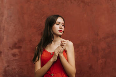 Porträt eines weiblichen Teenagers, der ein rotes Trägerkleid trägt und seitwärts vor einer Wand steht - TCEF00180