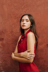 Portrait of female teenager wearing red strap dress in front of a wall - TCEF00181