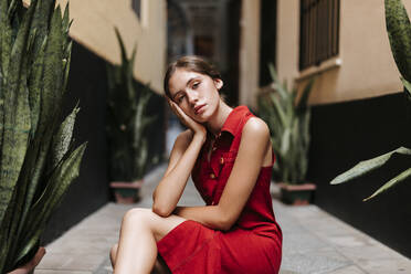 Portrait of female teenager wearing red strap dress in front of a wall - TCEF00184